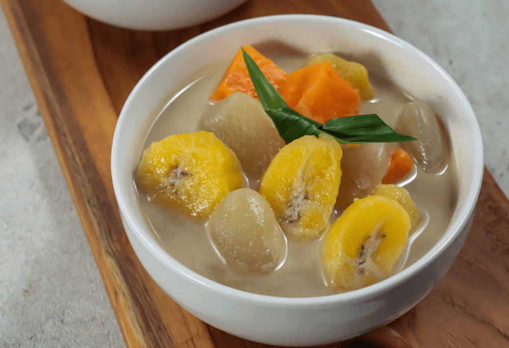 A bowl of golden che chuoi topped with roasted peanuts and coconut flakes, steam rising from the warm coconut milk base (Source: Canva)